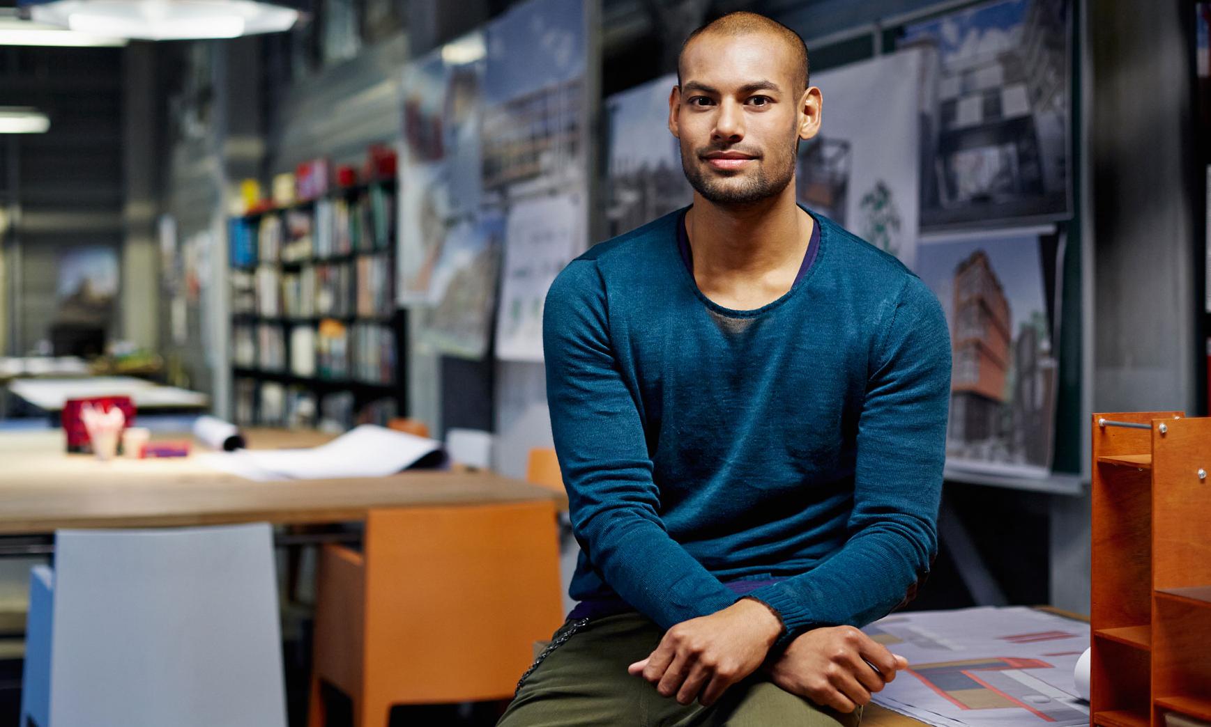 Man med blå tröja sitter på et skrivbord på ett arkitekt kontor